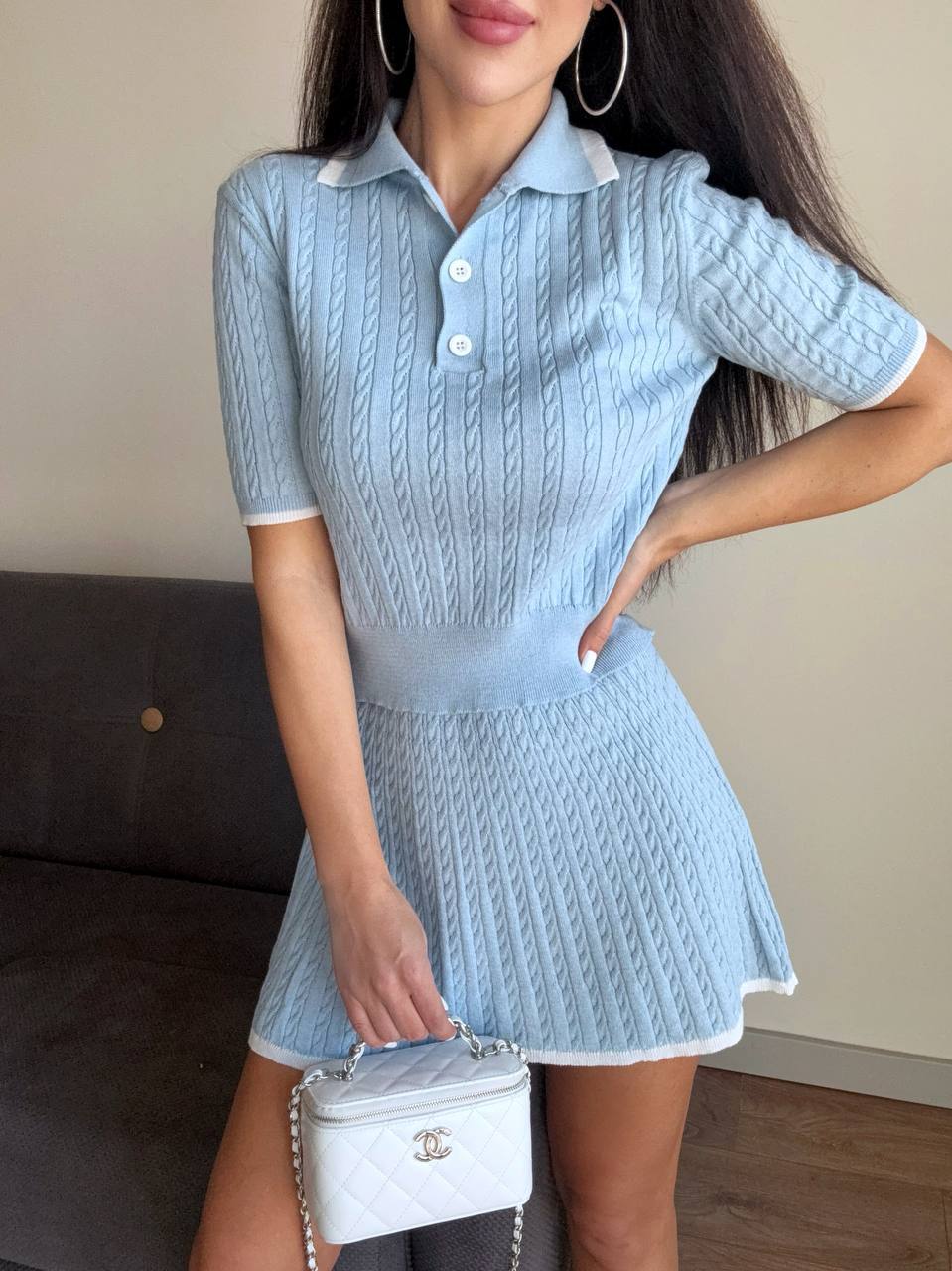 Woman wearing a light blue knitted dress with a white handbag indoors.