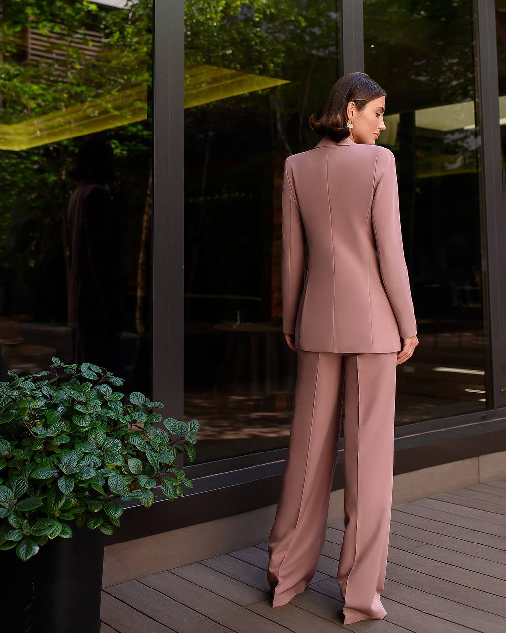 Woman in a pink suit standing on a wooden deck with greenery in the background