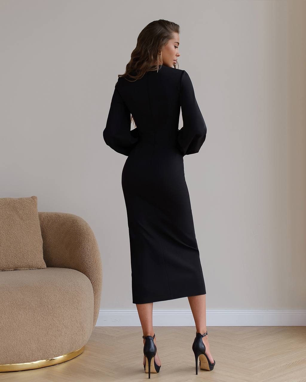 Woman in a black dress standing in a room with a beige sofa.