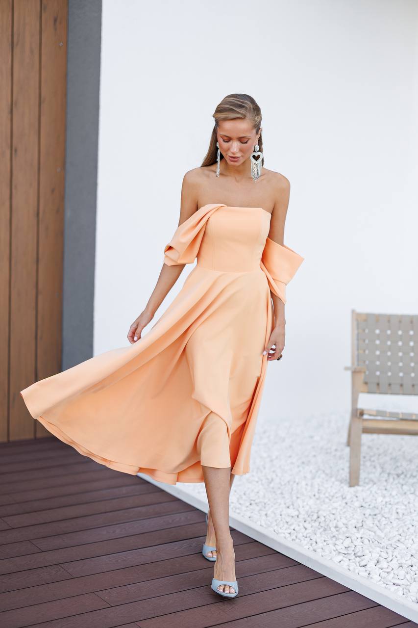 Woman wearing a peach off-shoulder dress on a wooden deck.