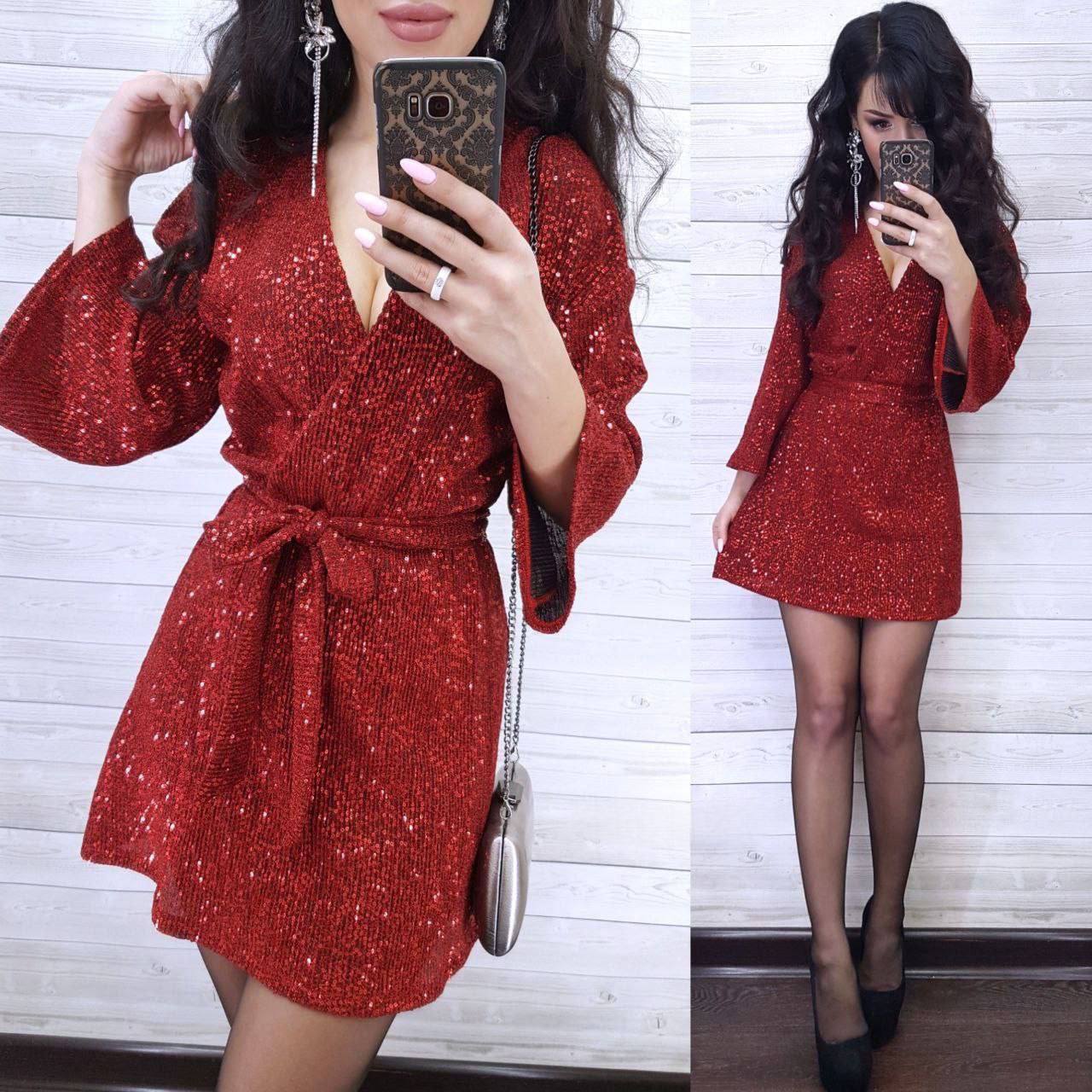 Woman wearing a red sequin dress taking a mirror selfie against a white wall.