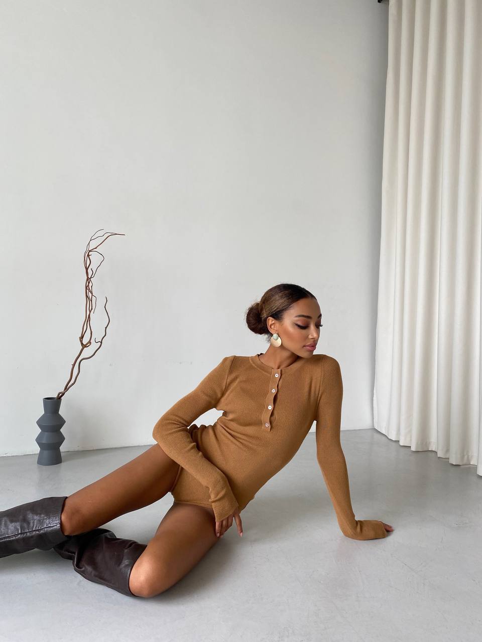 Woman in a brown dress sitting on the floor in a minimalistic room.