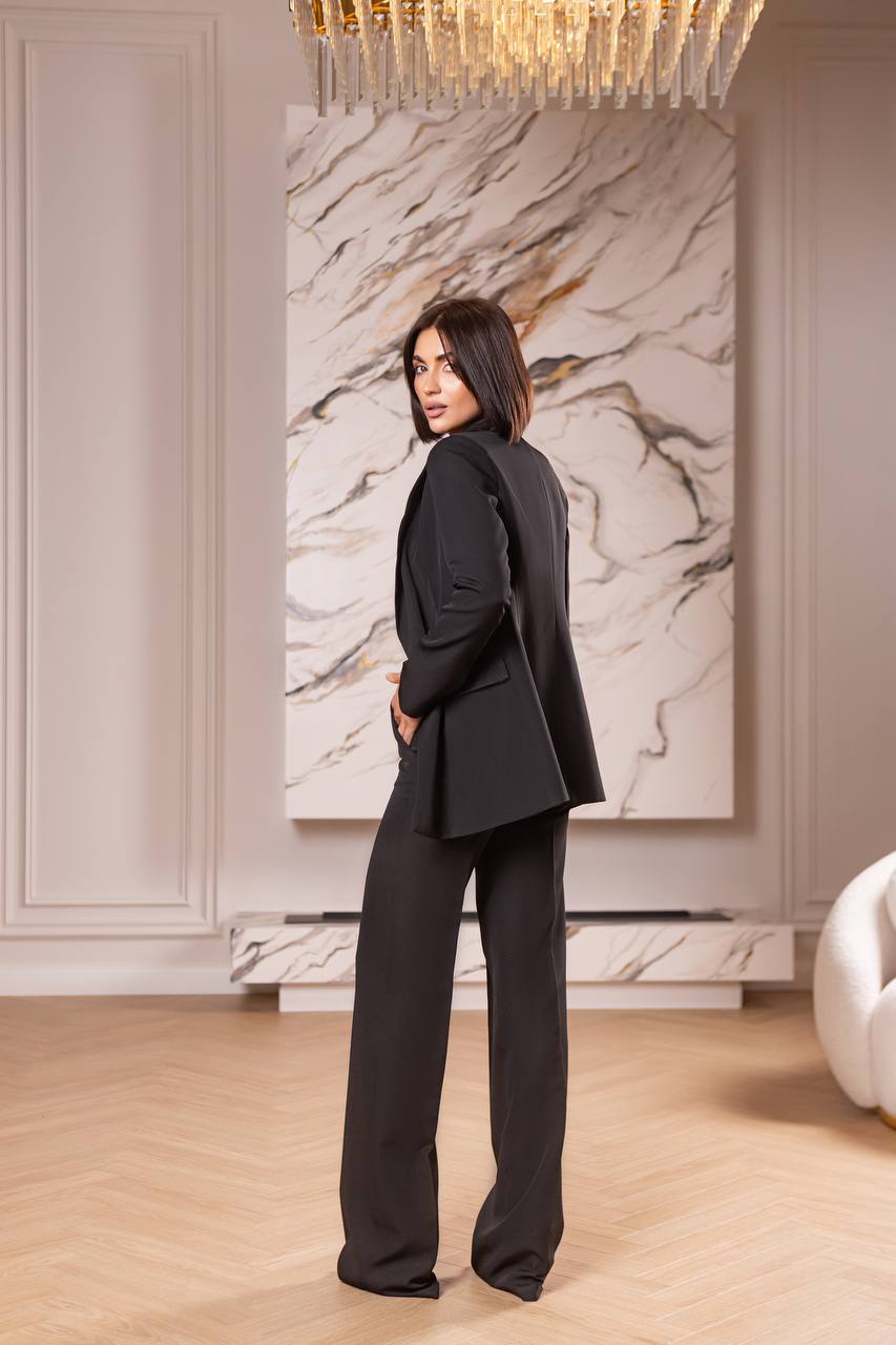 Woman in a black suit standing in a stylish room with marble wall and chandelier.
