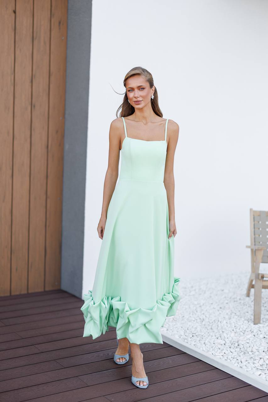 Woman wearing a light green dress with ruffled hem on a wooden deck.