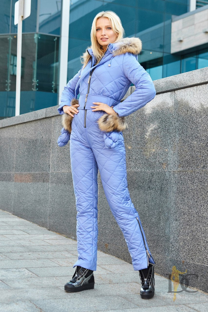 Woman in a blue winter outfit with fur trim standing against a modern building.