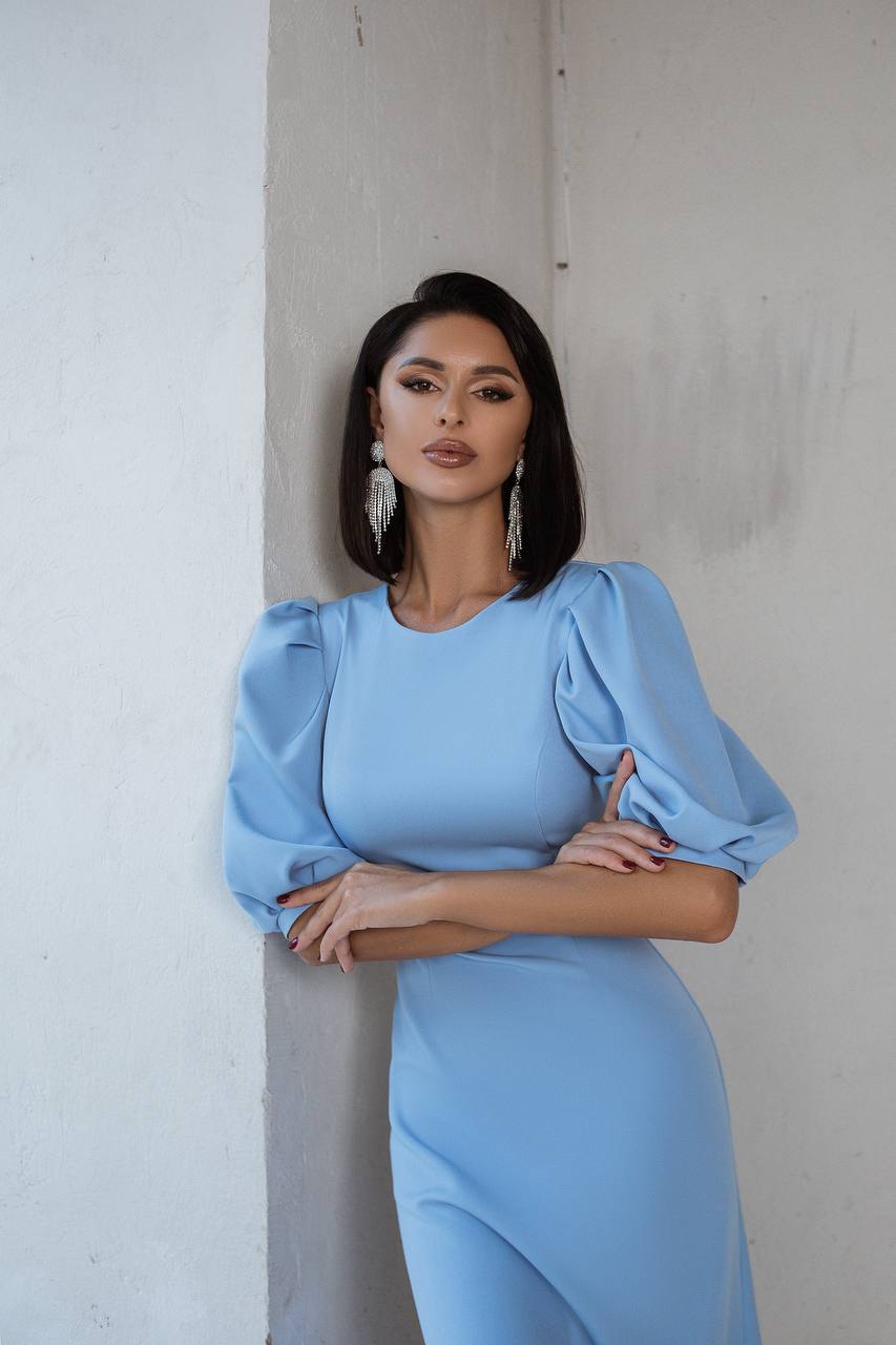 Woman wearing a light blue dress with puffed sleeves against a plain background