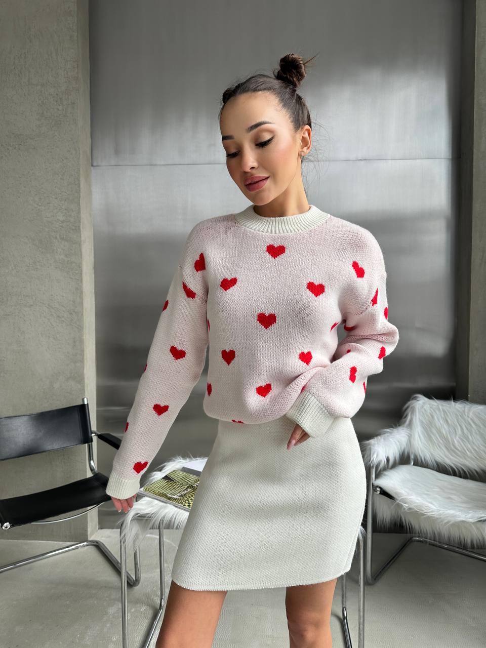 Woman wearing a pink sweater with red heart patterns in an indoor setting.