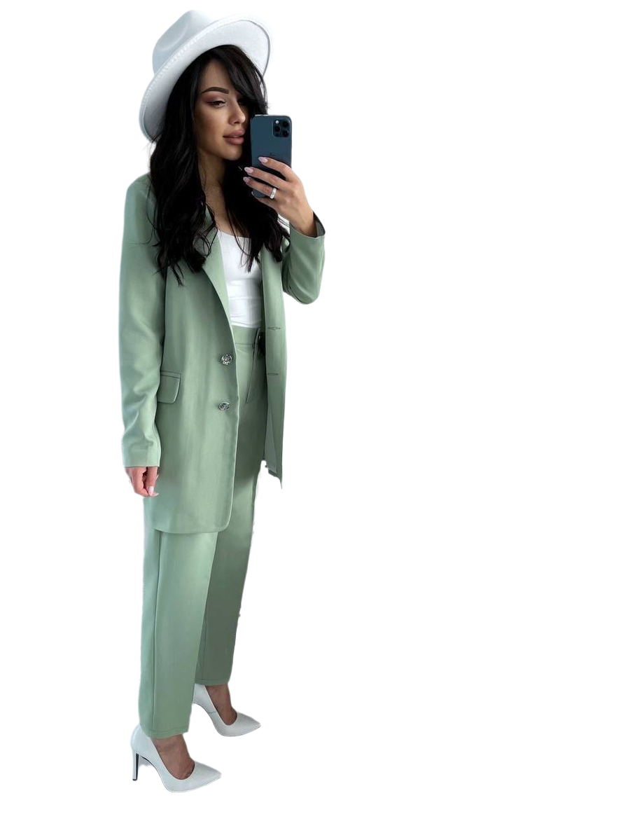 Woman in a green suit and white hat taking a selfie on a white background