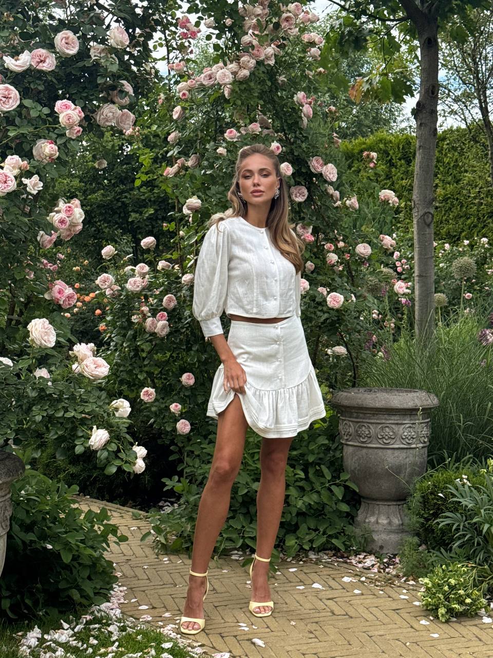 Woman in a white dress standing in a garden with floral arches