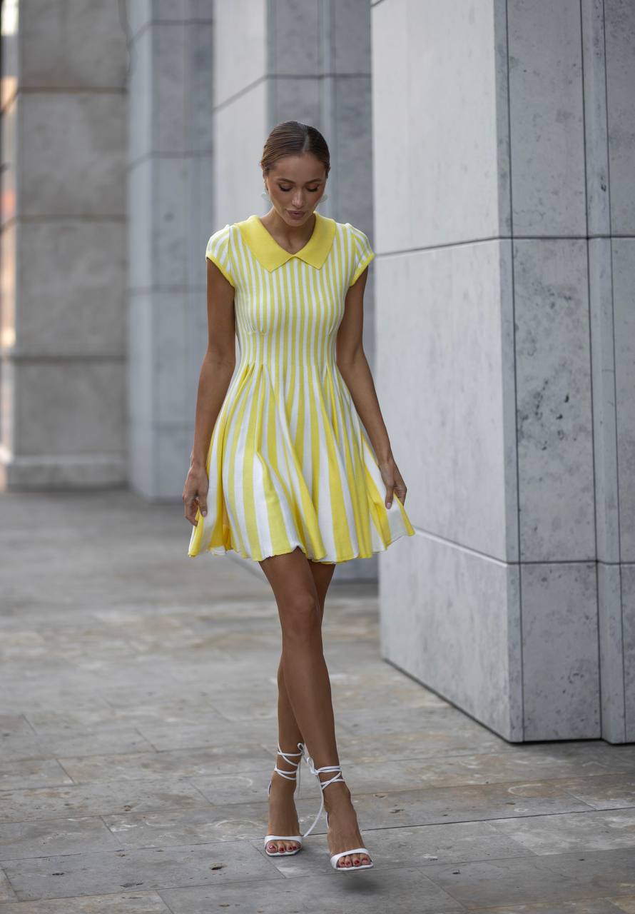 Woman wearing a yellow and white striped dress standing against a concrete wall.