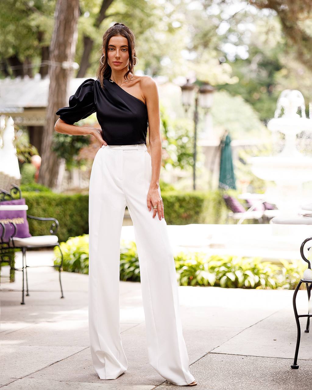 Woman wearing a black one-shoulder top and white pants in an outdoor setting