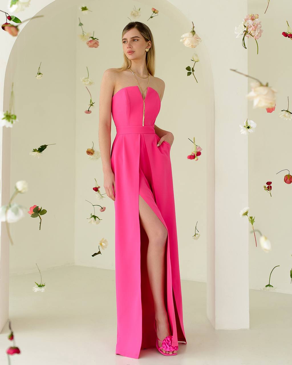 Woman wearing a pink strapless gown with a high slit in a decorated room.