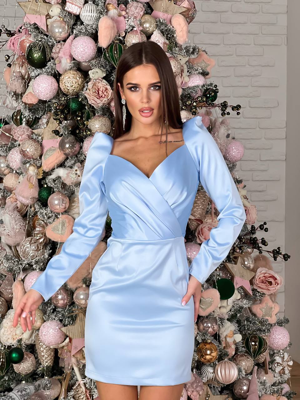 Woman in a light blue dress standing in front of a decorated Christmas tree.