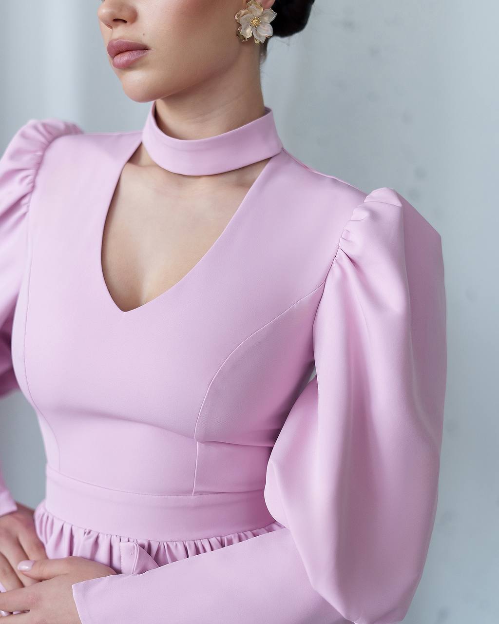 Close-up of a person wearing a pink dress with puffed sleeves against a light gray background