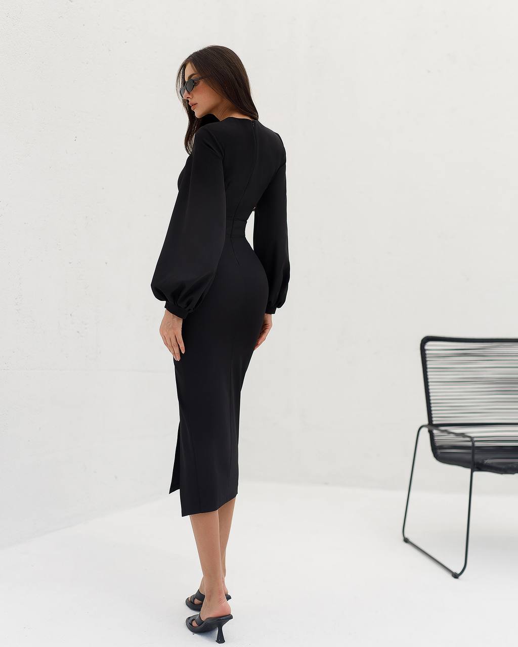 Woman wearing a black dress standing next to a black chair on a white background