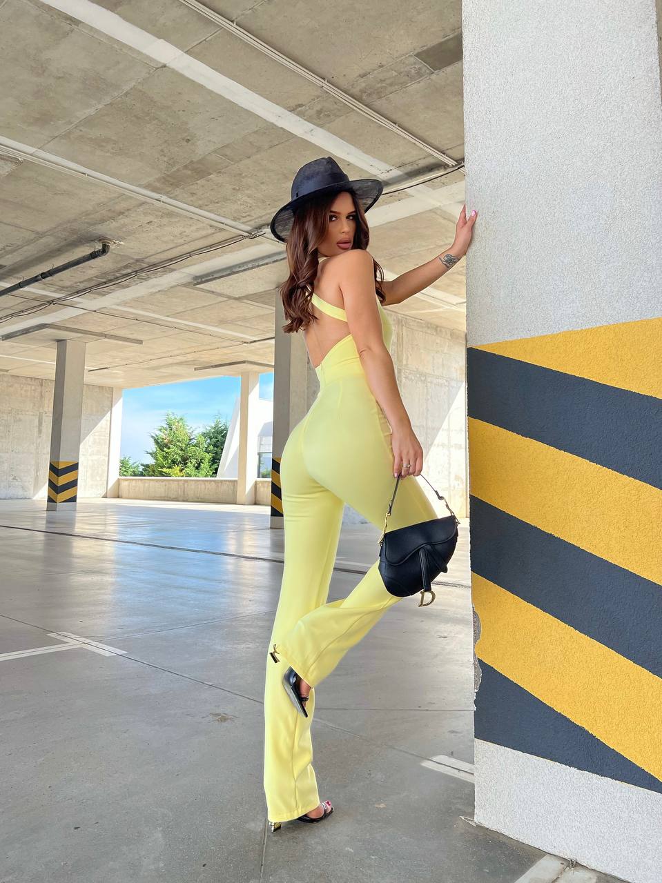 Woman in a yellow outfit and black hat standing in an underpass.
