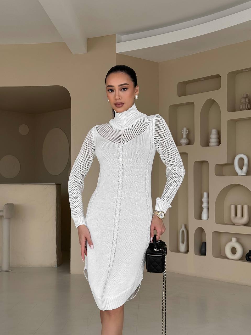 Woman in a white dress standing in a room with decorative shelves.