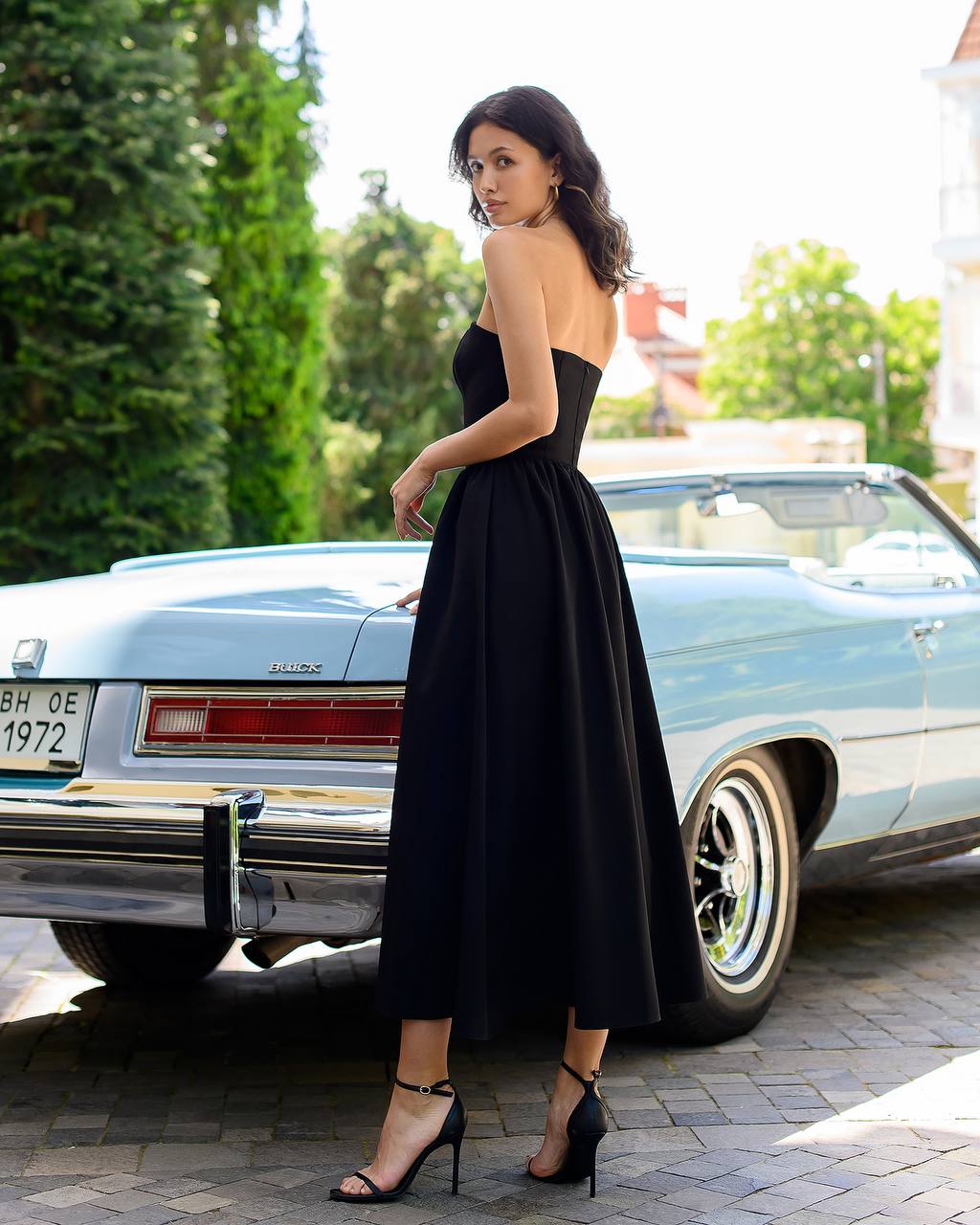Woman in a black dress standing next to a vintage car