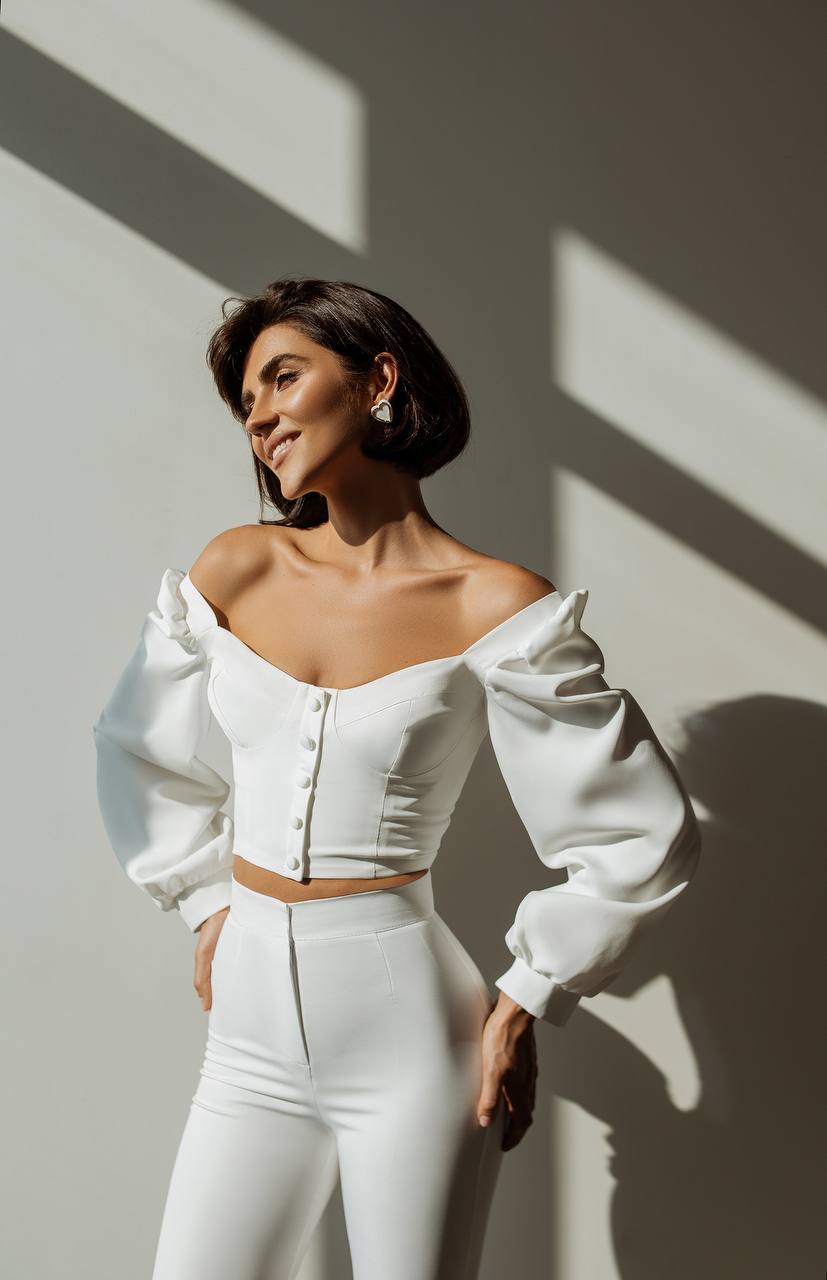 Woman wearing a white outfit with puffed sleeves against a light background