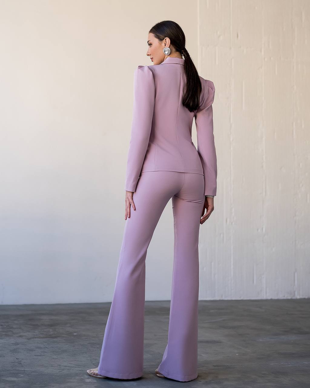 Woman wearing a lavender outfit with a high collar and flared pants against a plain background
