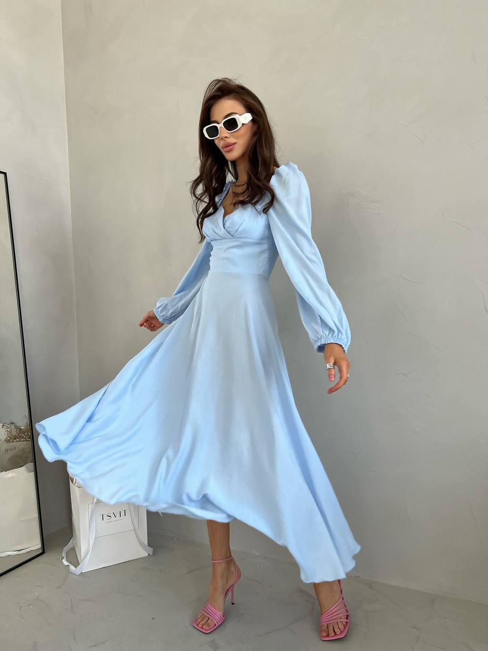 Woman wearing a light blue dress with long sleeves against a plain background