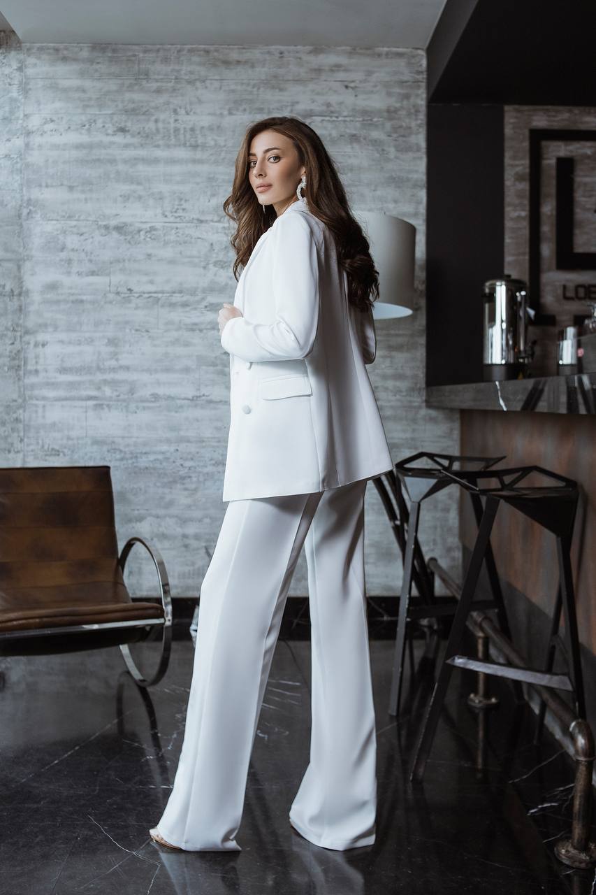 Woman in a white suit standing in a modern interior setting.
