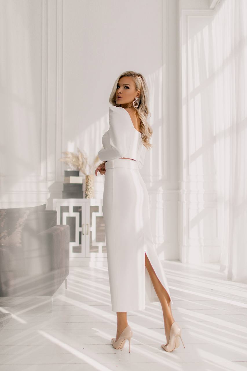 Woman in a white outfit standing in a modern, minimalistic room with white walls and furniture.