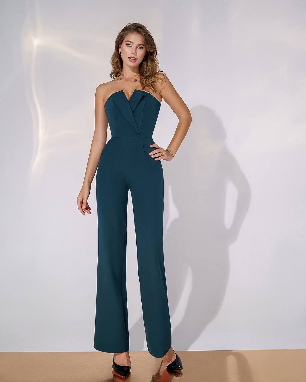 Woman wearing a teal strapless jumpsuit against a white background