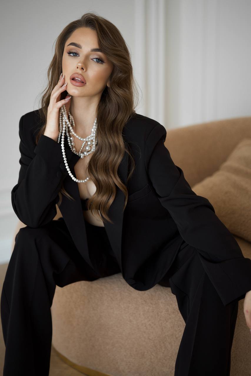 Woman in a black outfit with layered pearl necklaces sitting on a beige couch.
