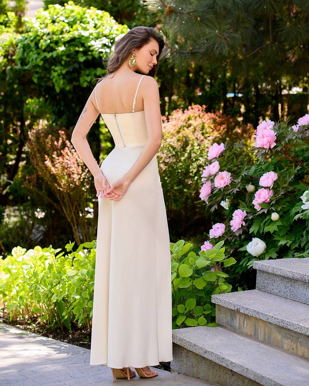 Woman in a white dress standing outdoors with greenery and flowers in the background