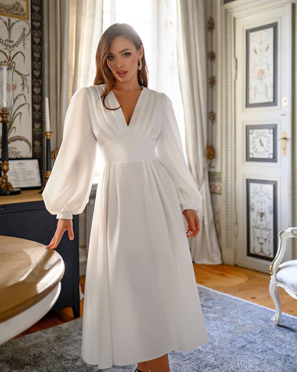 Woman in a white dress standing in a room with decorative elements.