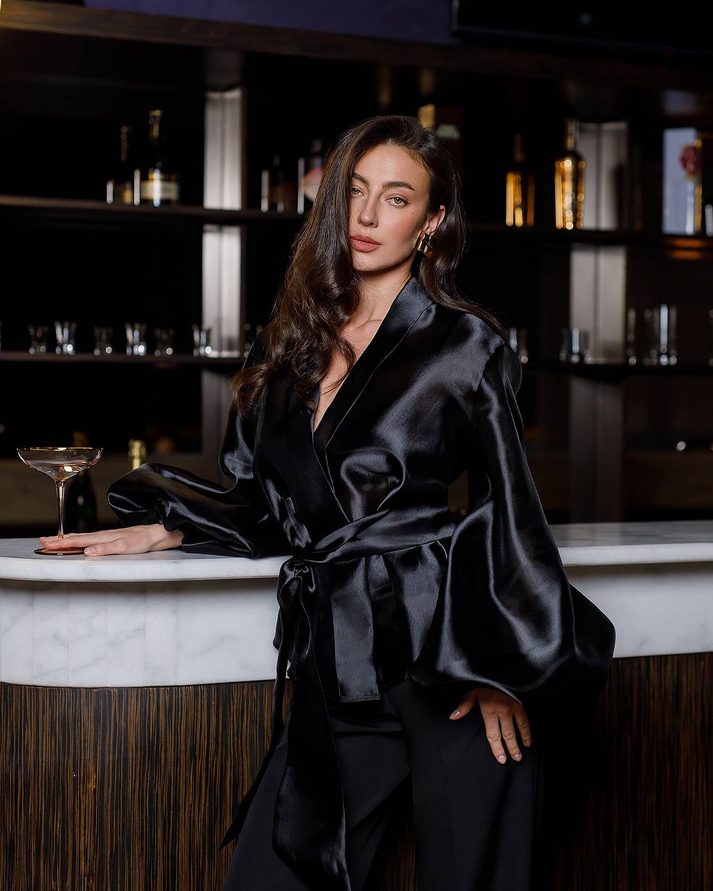 Woman in a black satin robe standing in a bar setting