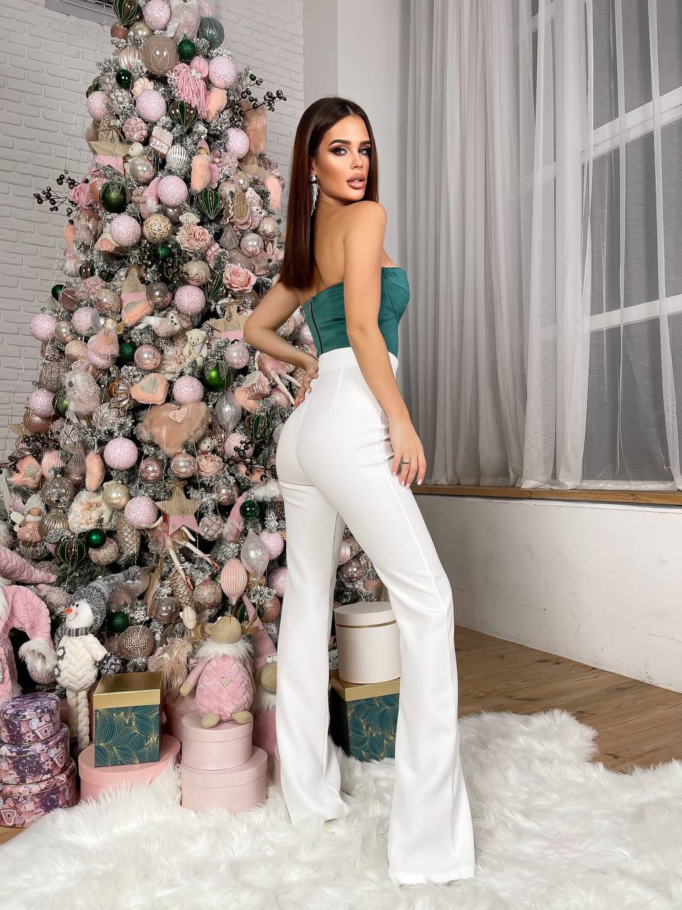 Woman in a teal top and white pants standing in front of a decorated Christmas tree.