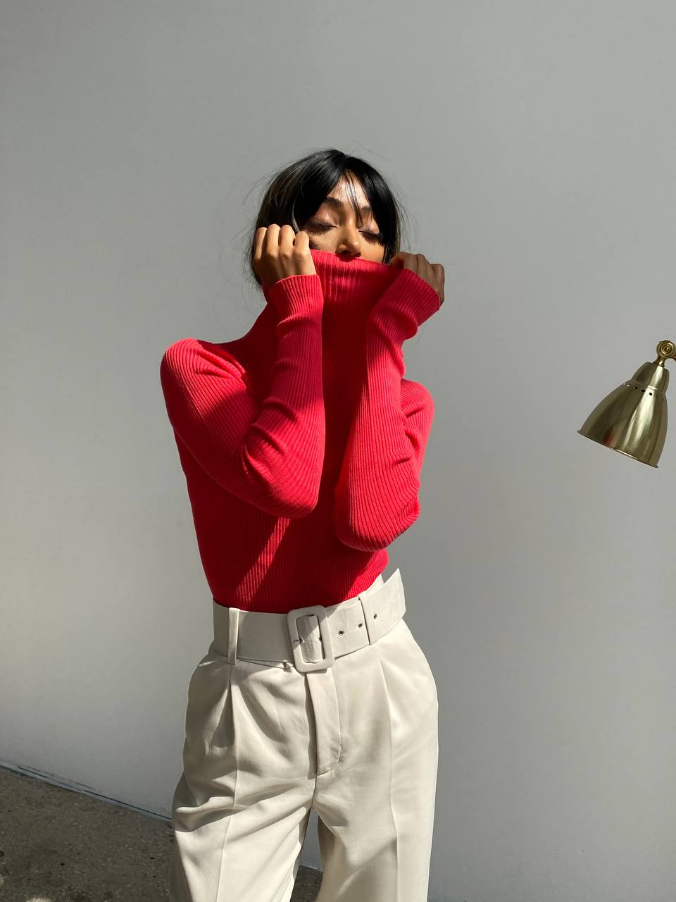 Person wearing a red sweater and beige pants against a plain wall.