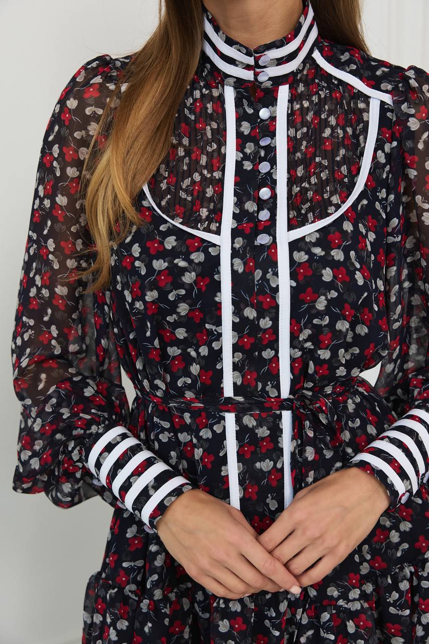 Person wearing a black floral dress with red and white accents on a plain background