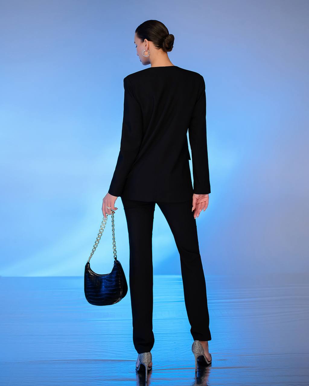 Woman in a black suit holding a black handbag on a blue gradient background