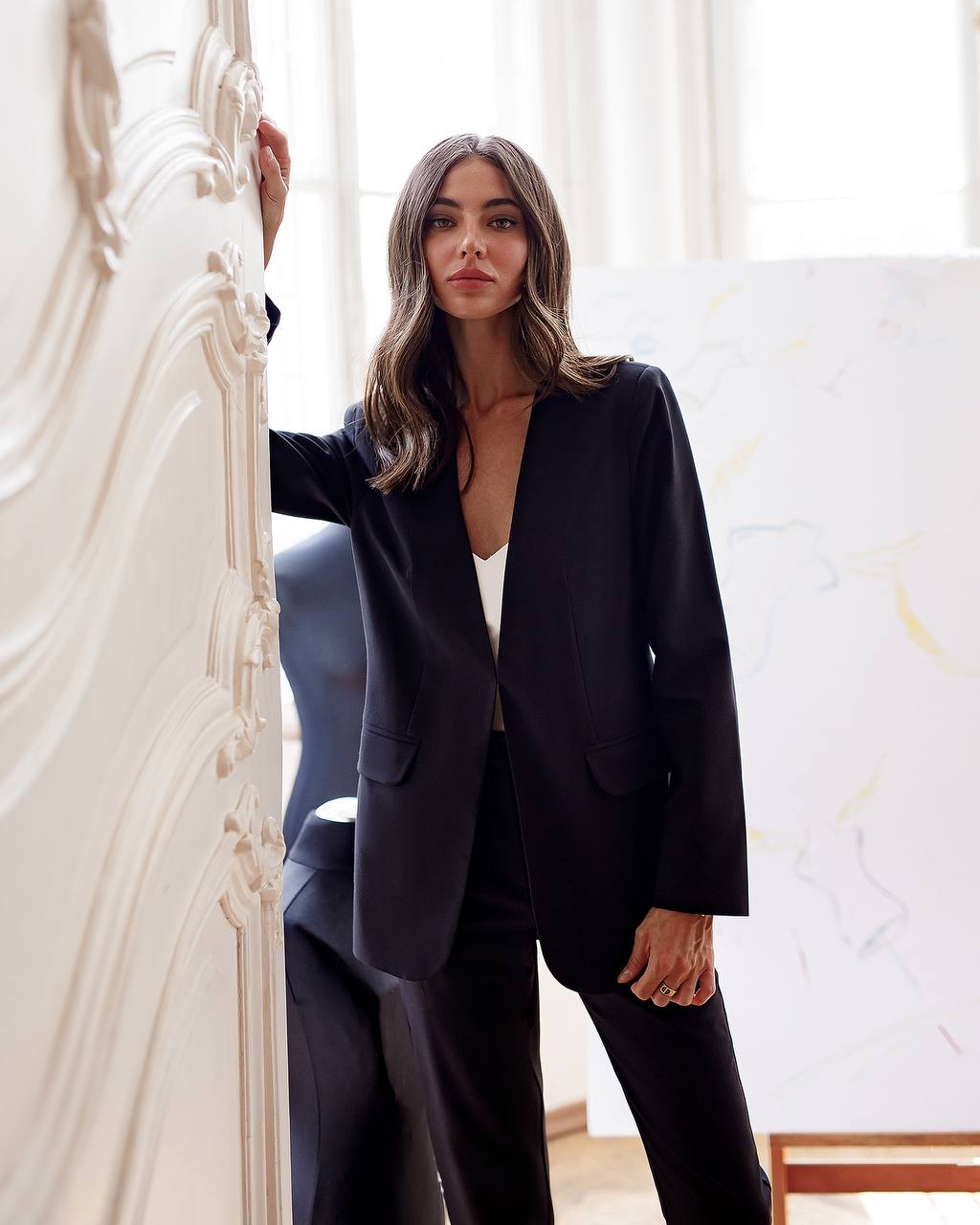 Woman wearing a black blazer over a white top in an elegant interior setting.