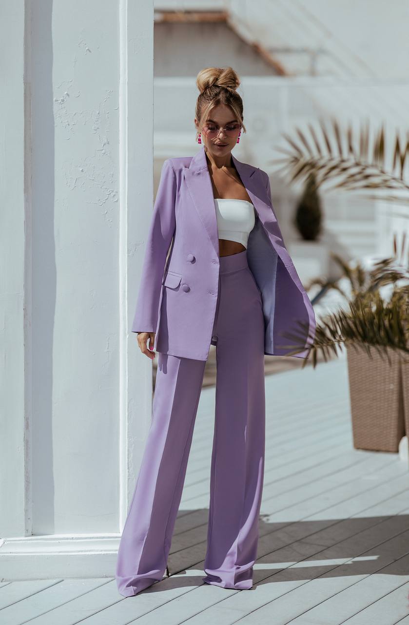 Woman in a lavender suit standing on a wooden deck with plants in the background