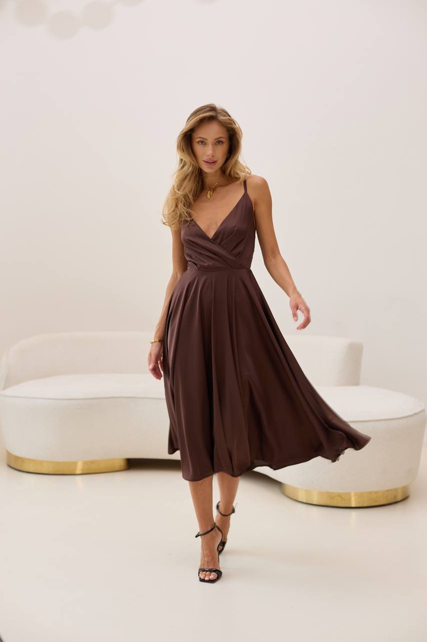 Woman in a brown dress standing in a minimalistic room with a white sofa.