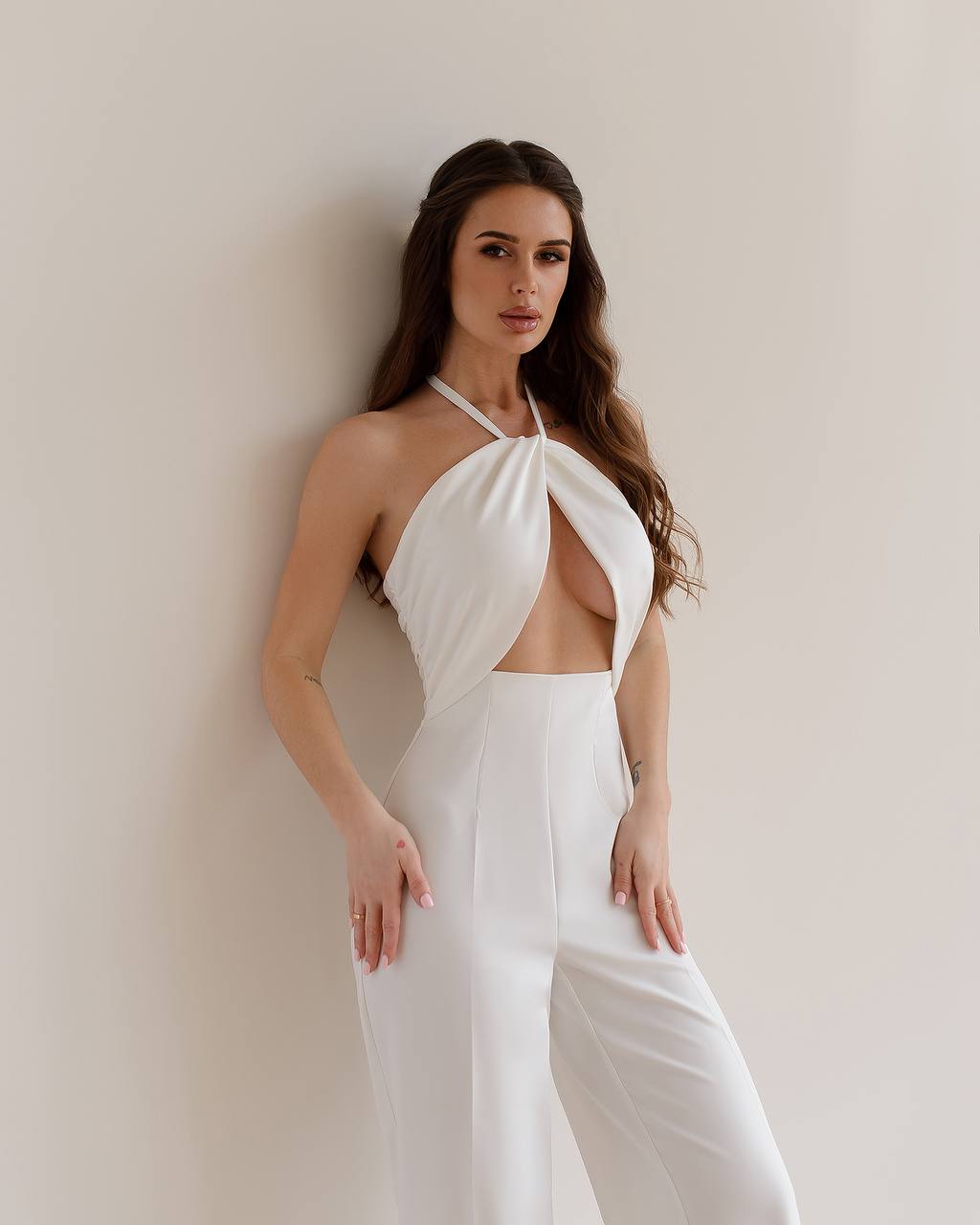 Woman wearing a white halter neck jumpsuit against a plain background