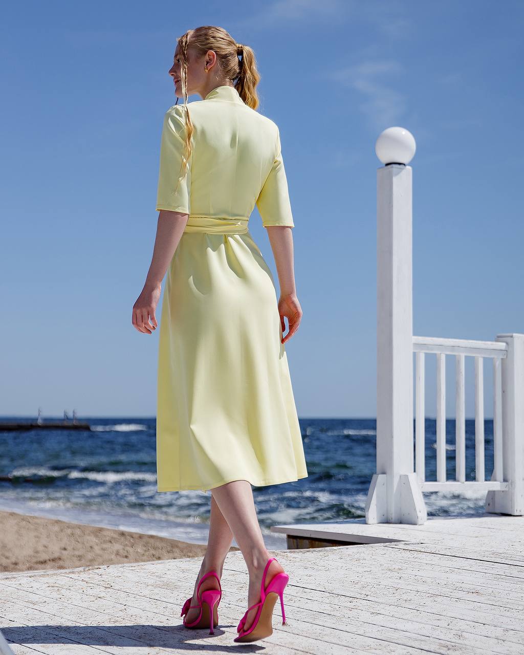 Woman in a yellow dress standing on a wooden deck by the ocean
