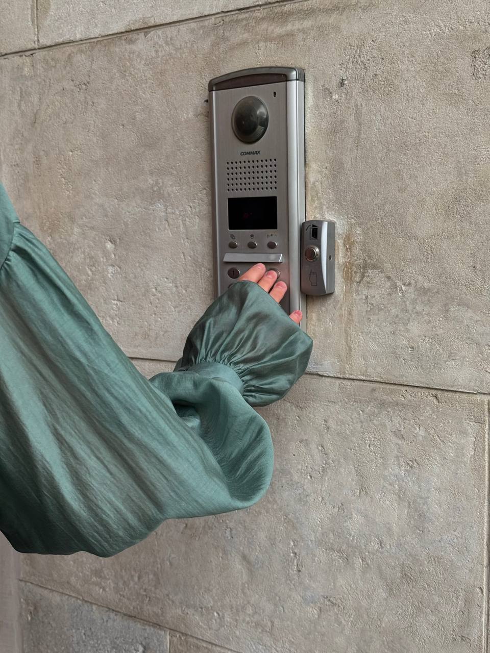 Person wearing a green glove pressing a doorbell on a stone wall.