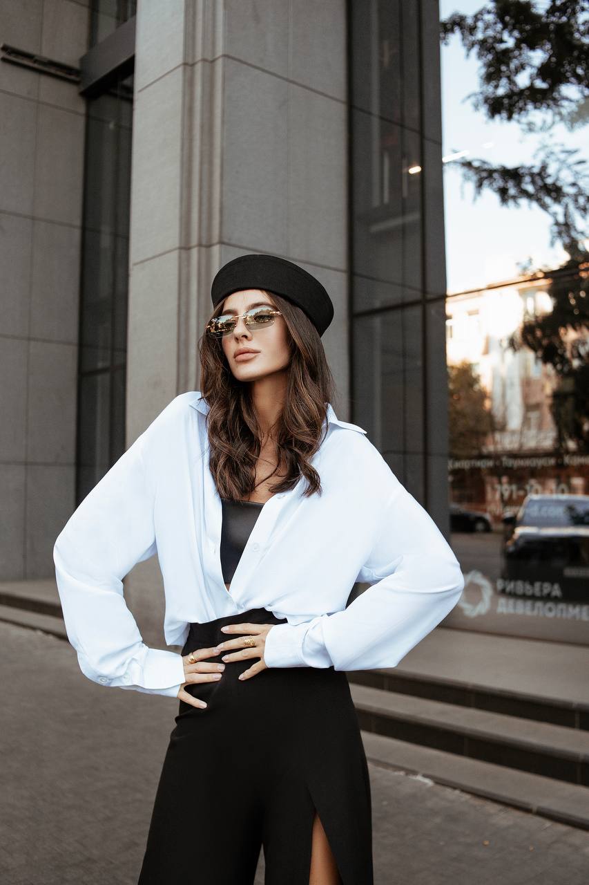 Woman wearing a white shirt and black skirt with sunglasses and a beret, standing on a city street.