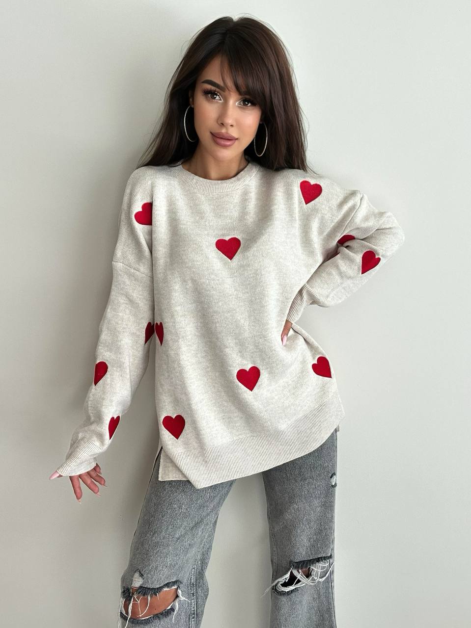 Woman wearing a white sweater with red heart patterns on a plain background