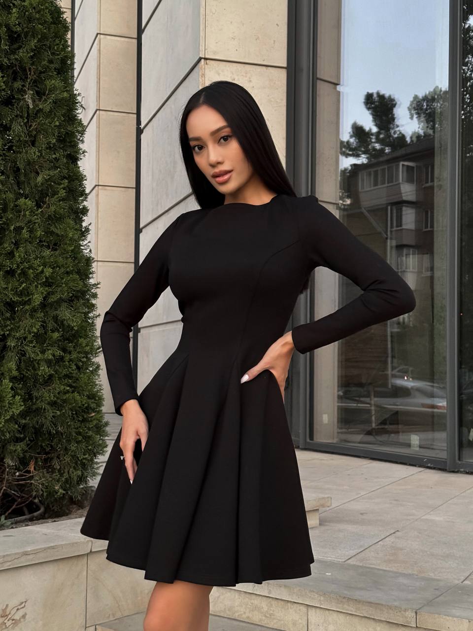 Woman wearing a black dress standing outdoors near a building.