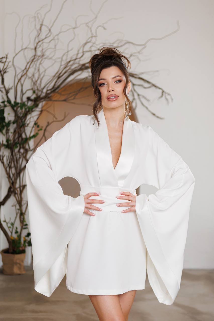 Woman wearing a white robe in a minimalistic room with plants.