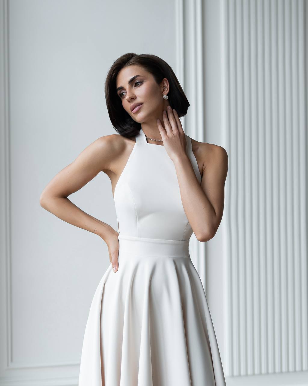 Woman wearing a white dress against a light gray wall