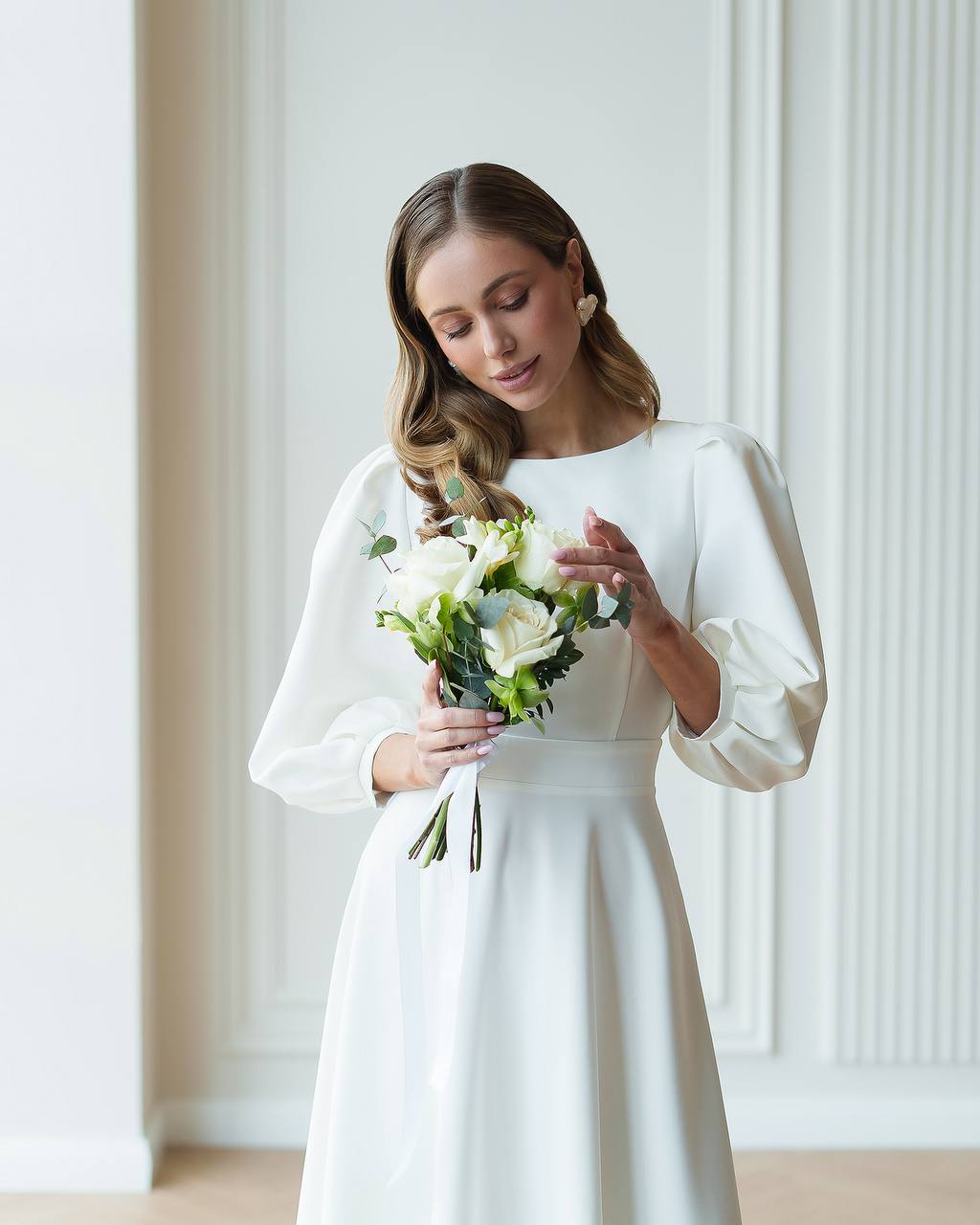 Woman in a white dress holding a bouquet of flowers in a minimalistic setting