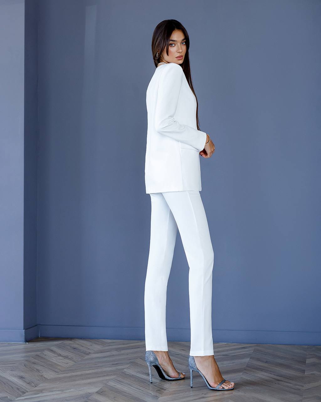 Woman wearing a white suit standing against a blue wall.