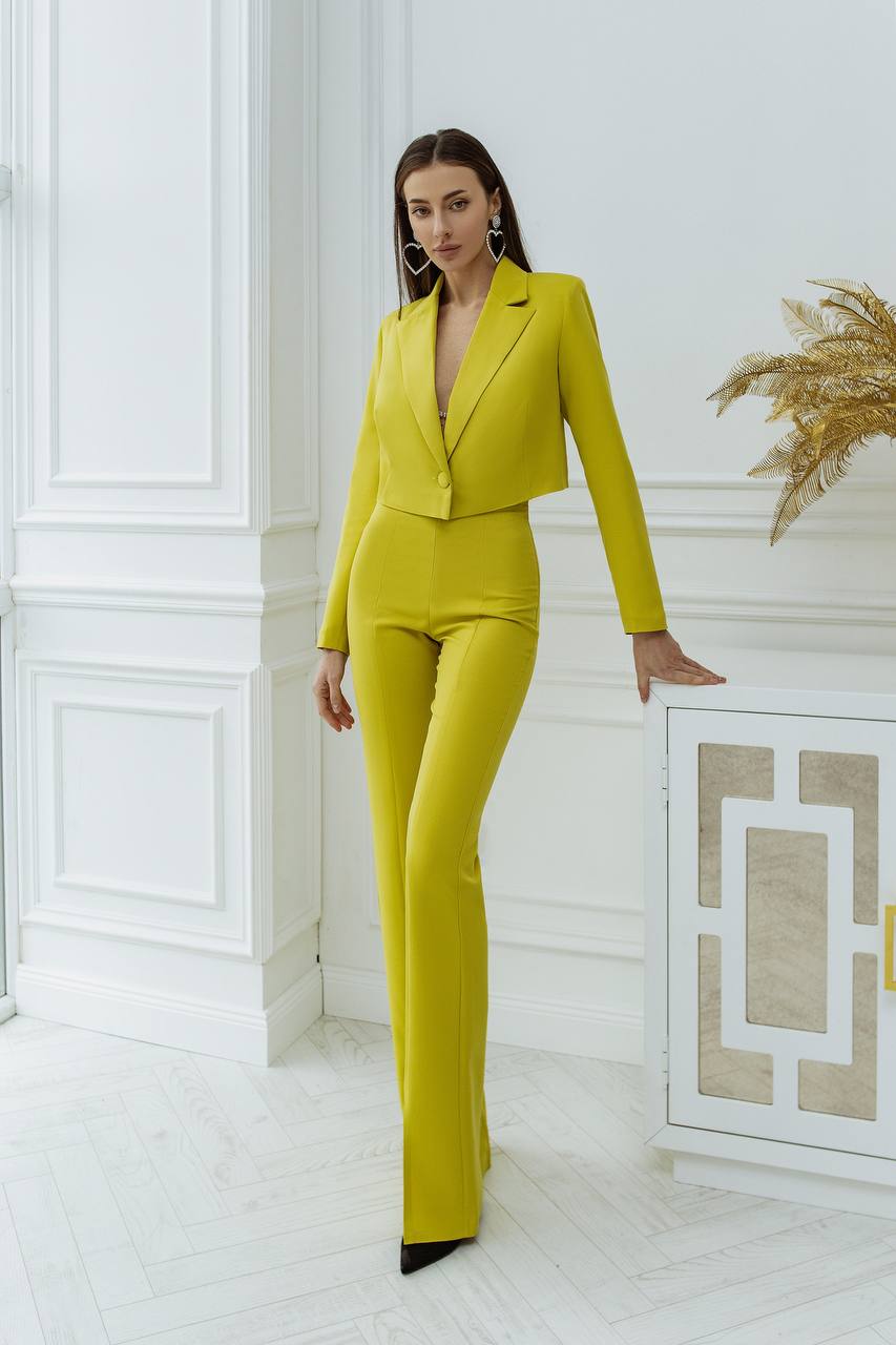 Woman in a bright yellow suit standing in a stylish interior setting.
